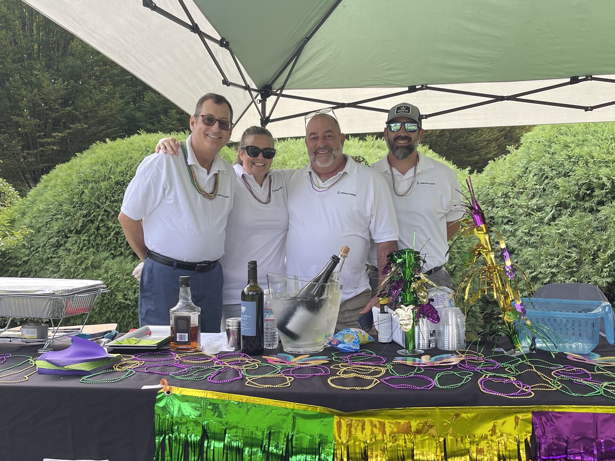 Four employees of Umpqua bank smile for a photo in front of a booth decorated for Mardi Gras