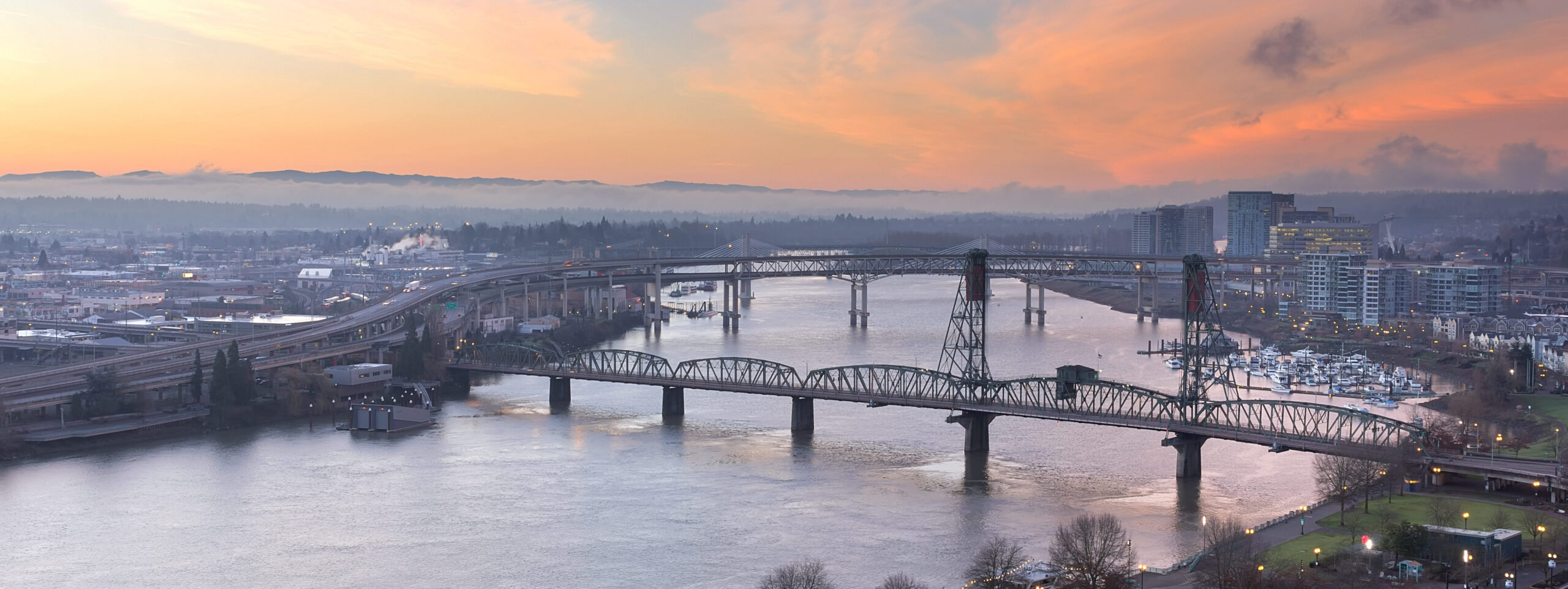 The Steel Bridge in Portland stretching across the city's river, with urban skyline in the background.