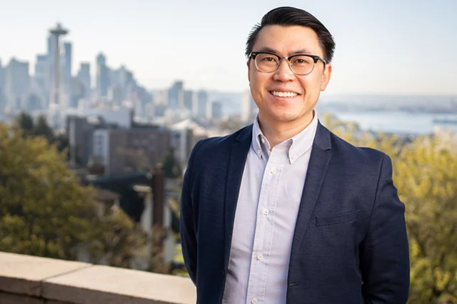 Man standing in front of blurred Seattle skyline on a sunny day.